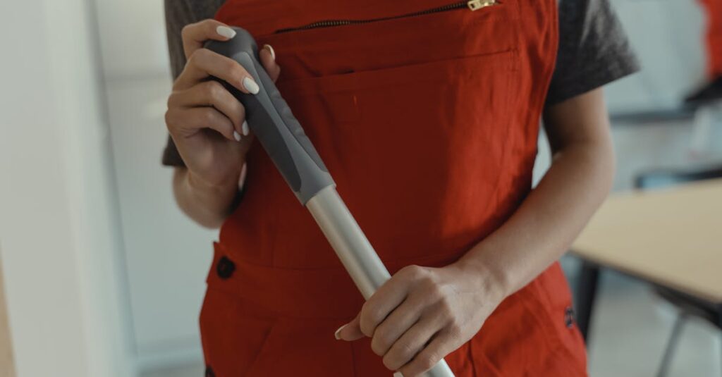 A woman in a red apron holding a mop handle, performing cleaning indoors.